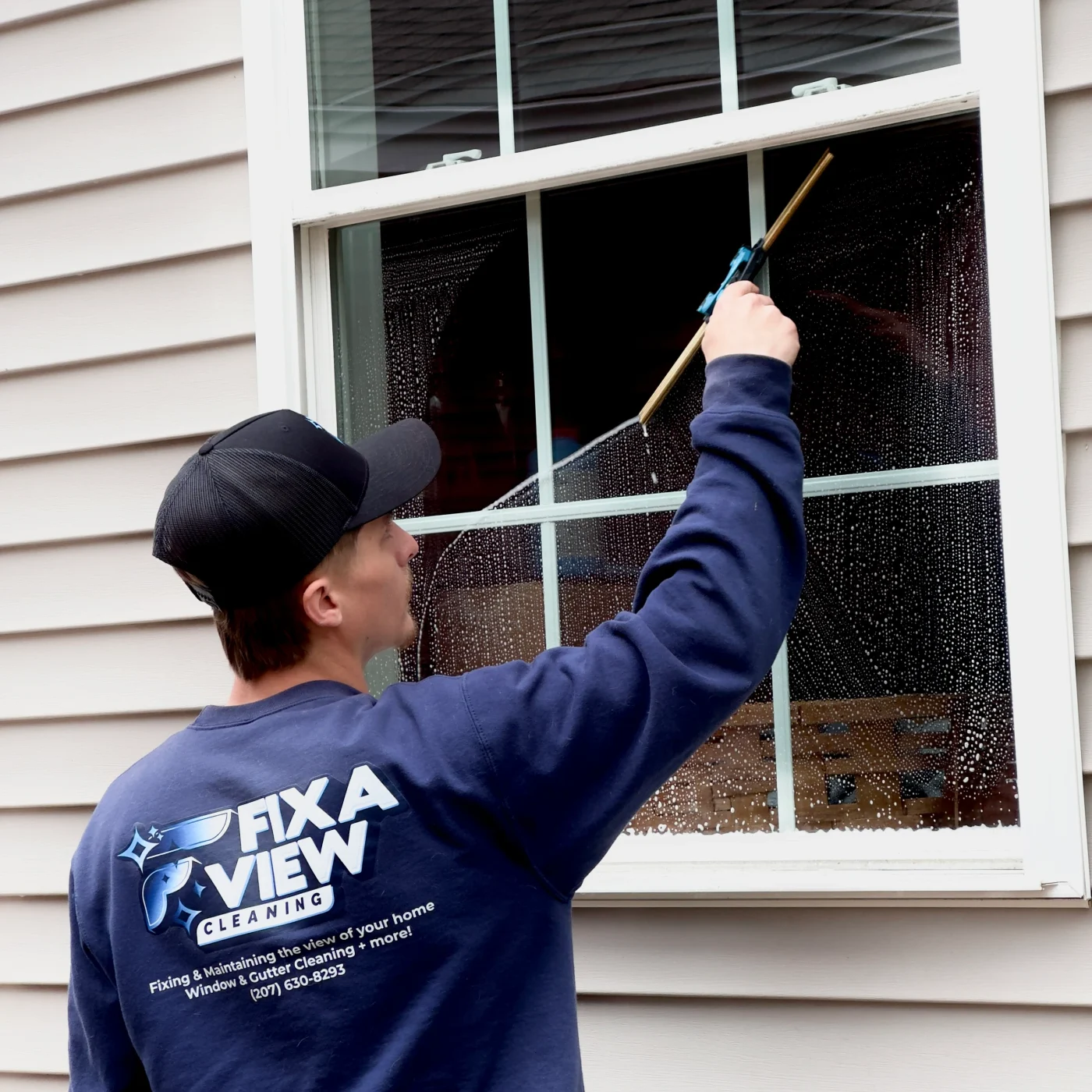 A Fix A View cleaner squeegeeing an exterior window mid-stroke