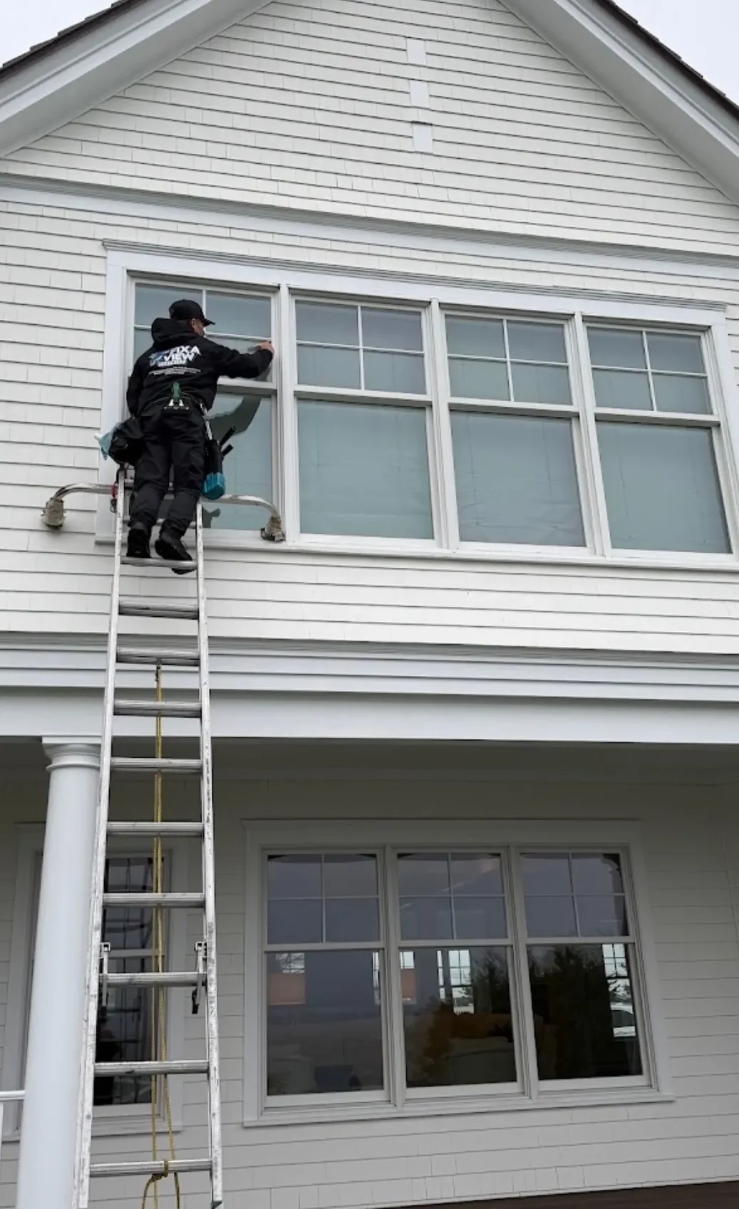 A Fix A View cleaner in branded uniform working a second story window from a ladder