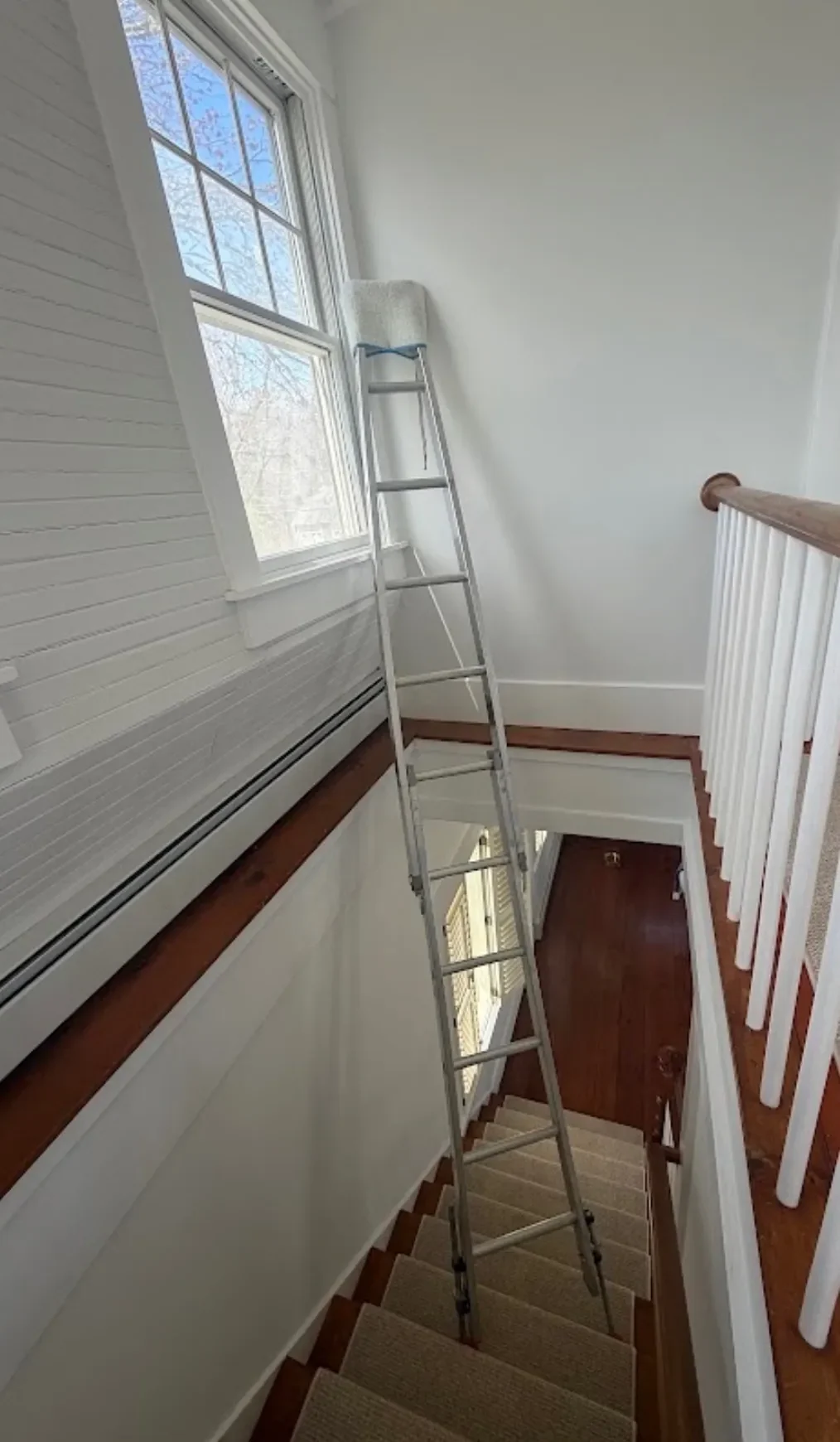 A ladder set over a staircase with padding on the top rail to protect the wall