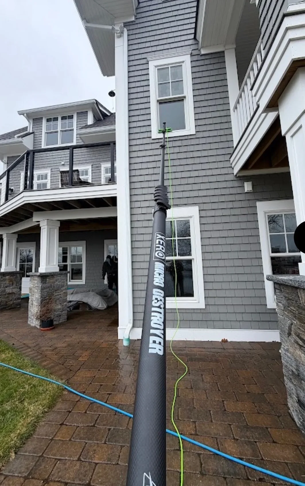 A water-fed pole reaching the upper windows of a gray shingled coastal home